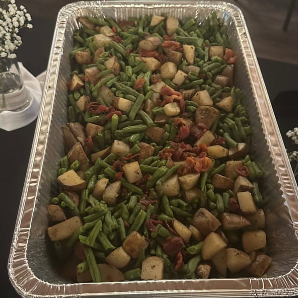 Roasted potatoes, green beans, and sun-dried tomatoes in a large aluminum catering pan.
