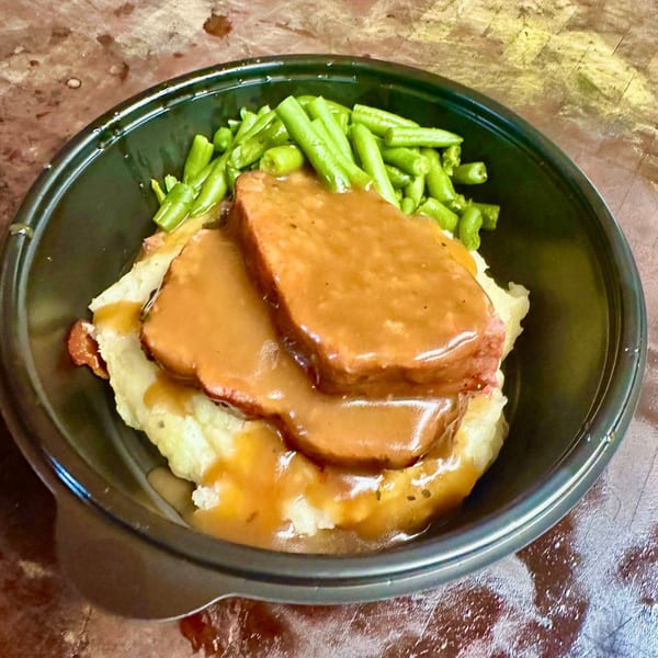 Brisket BBQ meatloaf with gravy, mashed potatoes, and green beans in a black bowl.