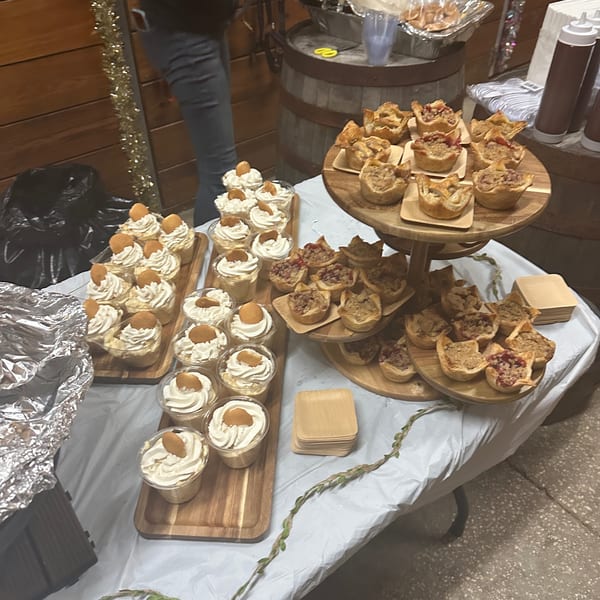 Dessert table with banana pudding cups and mini pecan pies on wooden trays at Briskets BBQ.