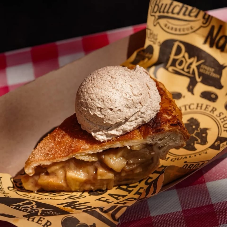 A slice of Briskets BBQ apple pie with a scoop of ice cream on branded paper.