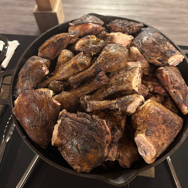 A large cast iron skillet filled with many pieces of dark, crispy grilled chicken.