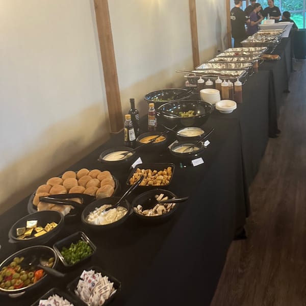 A long buffet table with various dishes, including rolls, salads, and hot food in foil pans.