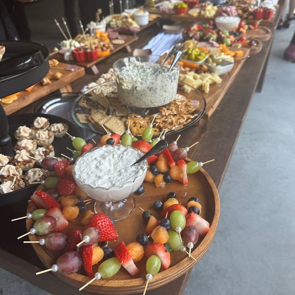 A long table filled with various appetizers, including fruit skewers, dips, crackers, and cheese.