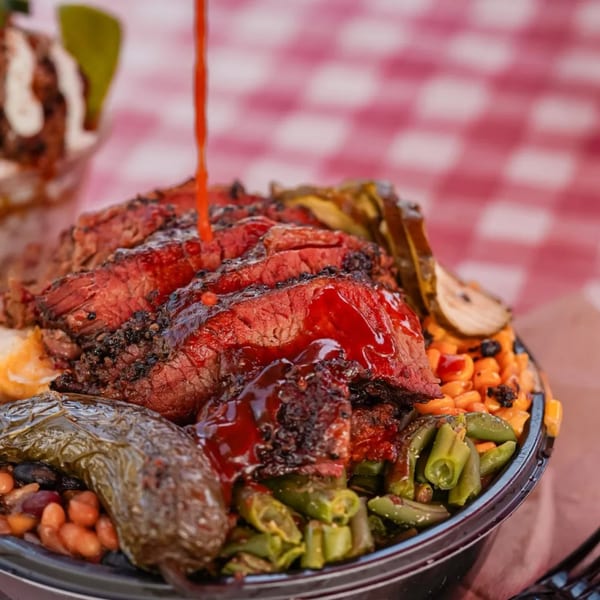 Brisket BBQ bowl with sliced brisket, beans, corn, green beans, and a whole roasted pepper, drizzled with sauce.