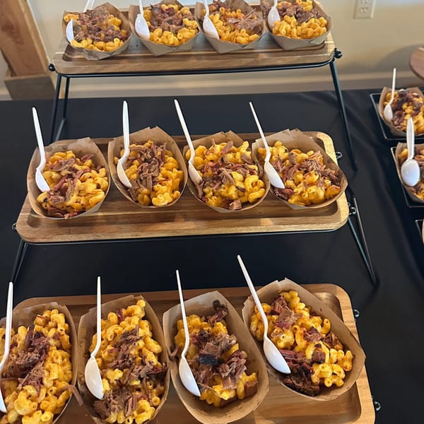 Rows of mac and cheese topped with pulled pork in individual paper boats on a tiered serving stand.