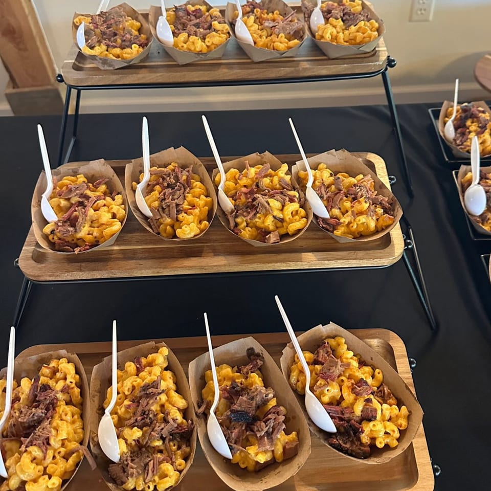 Rows of mac and cheese topped with pulled pork in individual paper boats on a tiered serving stand.