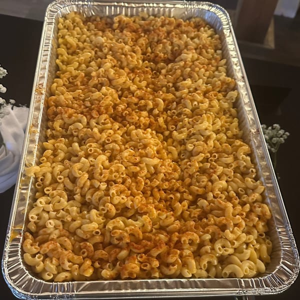 A large aluminum tray filled with creamy macaroni and cheese, sprinkled with paprika.