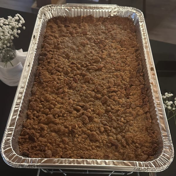 A large rectangular aluminum pan filled with a brown crumble dessert, possibly apple or peach cobbler.