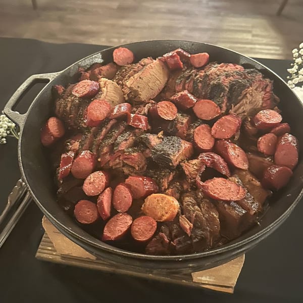 A cast iron pot filled with sliced brisket and sausage, ready to be served.