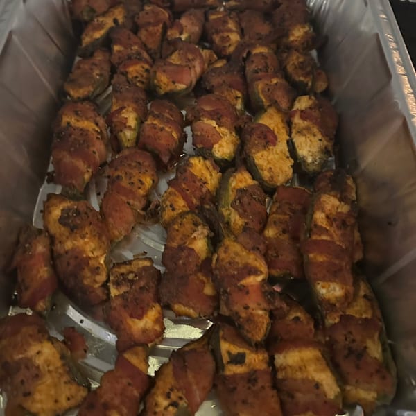 Close-up of numerous bacon-wrapped jalapeño poppers in a metal serving tray.