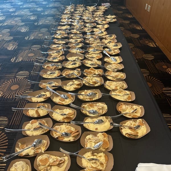 Rows of individual banana pudding cups with vanilla wafers and spoons on a black tablecloth.