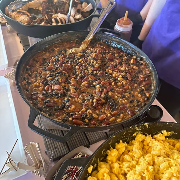 Close-up of a large cast iron pot filled with Briskets BBQ baked beans, with mac and cheese below.